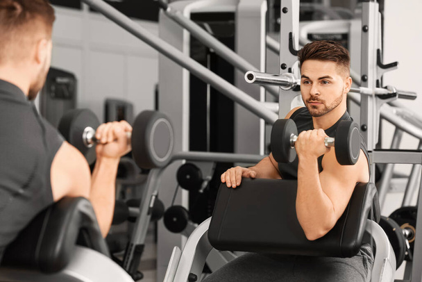 Sporty young man training with dumbbells in gym - Zdjęcie, obraz
