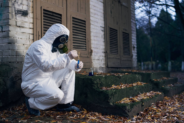 Scientist wearing protective coverall, gas mask and gloves. Worker making expertise using glass flask and local samples, copy space - Photo, Image