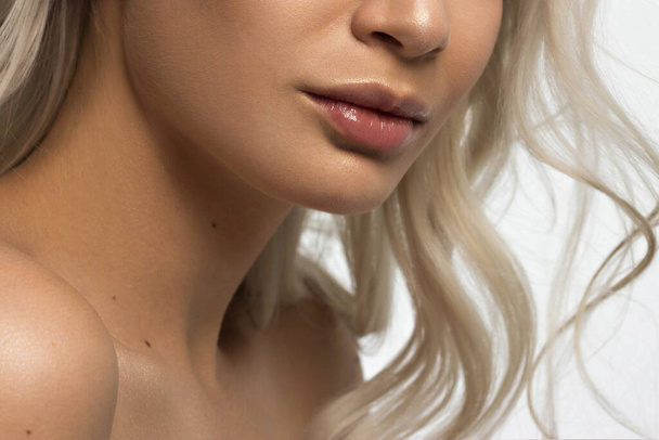 Sexual full lips. Natural gloss of lips and woman's skin. The mouth is closed. Increase in lips, cosmetology. Pink lips and long neck. Gentle pure skin and wavy blonde hair. - Fotó, kép