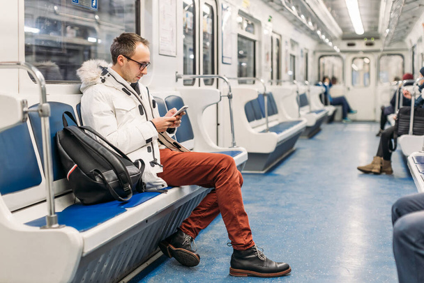 Handsome adult man in glasses with black backpack riding in subway train. In hands male hold smartphone. Social medias swallowed him up and he missed his stop. Internet addiction. Copy space. - Фото, зображення