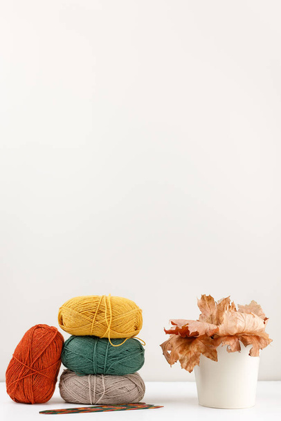 パステルカラーの糸の赤、緑、黄色、ベージュの爪と多色の木製の編み針の垂直写真。乾燥したカエデの葉の近くの花瓶。針仕事とレジャーの概念。スペースのコピー. - 写真・画像