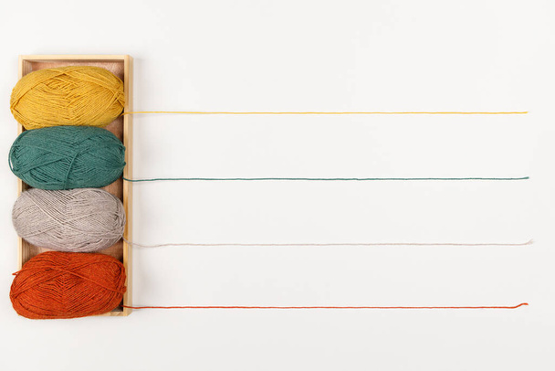 Gele, groene, beige en rode bollen garen van pastelkleuren in houten dienblad. De draden vormen een regel voor de tekst. Begrepen, ruimte. Naald- en vrijetijdsconcept. Vrouwelijke hobby. Sjabloon voor uw ontwerp - Foto, afbeelding