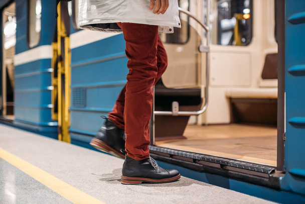 Dobře oblečený muž v černých botách, červených kalhotách a bílé bundě nastupuje brzy ráno do vlaku metra. Levá noha je rozmazaná. Uzavřete fotku. Veřejná doprava a mobilita v městské koncepci. - Fotografie, Obrázek