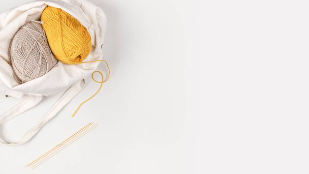 Yellow and beige clews of yarn in a textile bag. From the yellow skein of yarn a thread runs to the bamboo knitting needles. Copy space. Needlework and leisure concept. Template for your design. - Photo, Image