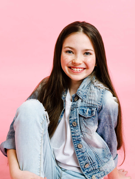 Portrait of adorable smiling little girl child in jeans isolated on a pink background - 写真・画像