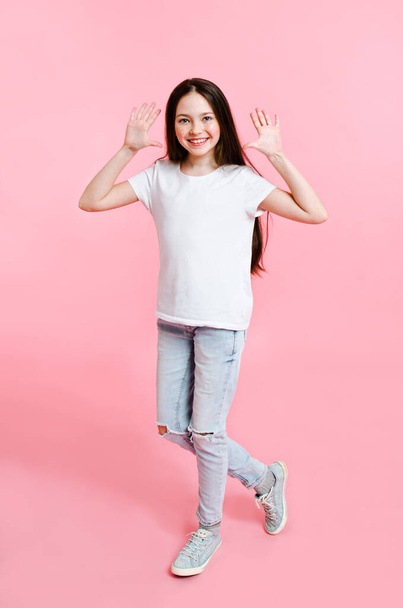 Portrait of adorable smiling little girl child in the white t-shirt having fun isolated on a pink background - Foto, Bild