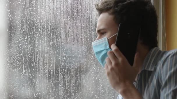 Junger Mann mit Gesichtsmaske, krank mit COVID-19, unter Quarantäne in einem Krankenhaus, beunruhigt am Telefon.  - Filmmaterial, Video