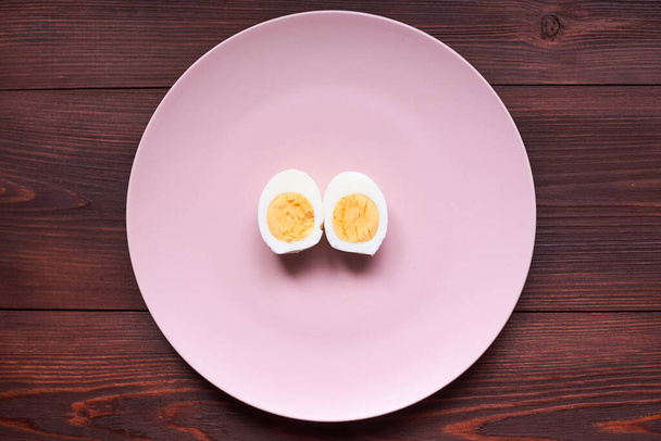 Boiled chicken egg cut into two halves on a pink plate. - Фото, зображення