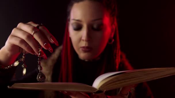 Witch with amulet reading magic book on black background - Footage, Video