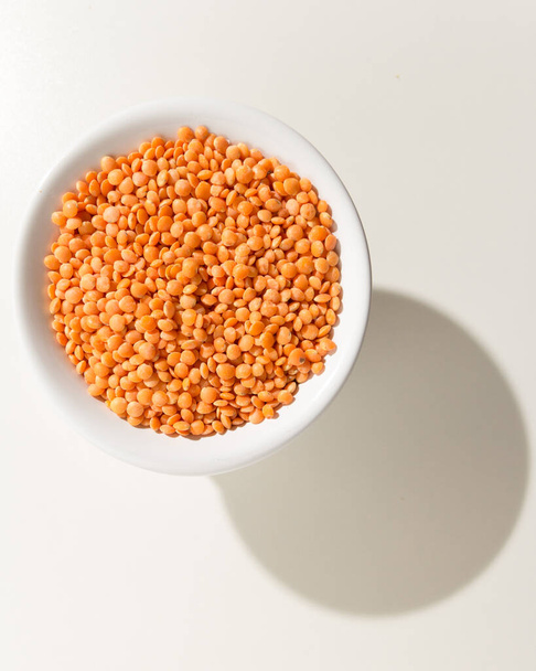 Lens culinaris è il nome scientifico del legume turco della lenticchia rossa. Conosciuto anche come Lentilha Vermelha (portoghese). Cereali in una ciotola. Ombra sul tavolo bianco
. - Foto, immagini