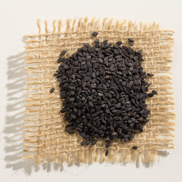 Sesamum radiatum is scientific name of Benniseed. Also known as Black Sesame, Gergelim Preto (portuguese) and Sesamo negro (spanish). Pile of grains, isolated white background. Close up of grains over burlap. - Фото, зображення