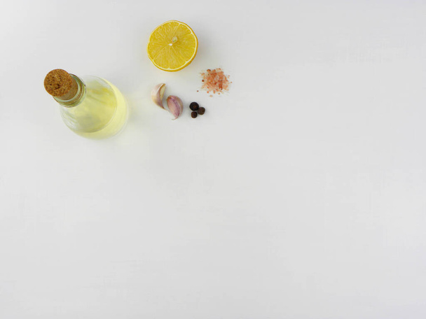 limão meio maduro, óleo em uma garrafa de vidro, dois dentes de alho, grãos de pimenta e sal rosa em um fundo branco
                                - Foto, Imagem