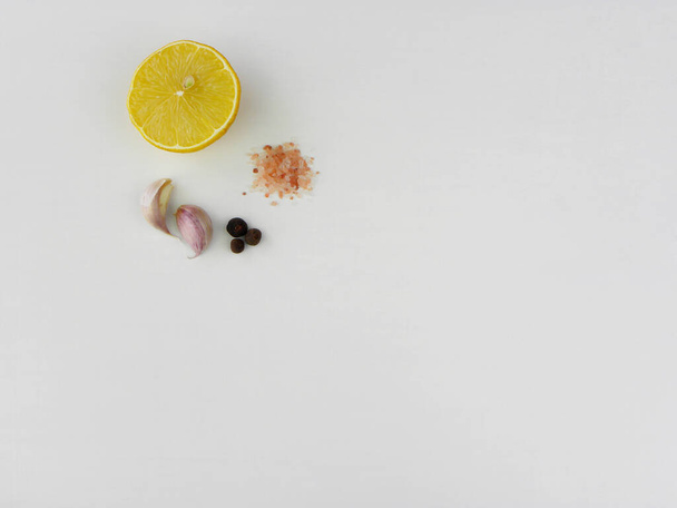     half ripe lemon, two cloves of garlic, grains of pepper and pink salt on a white background                            - Zdjęcie, obraz