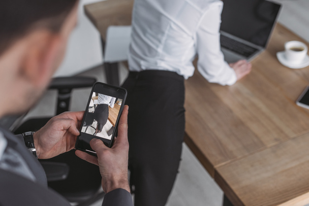 επιλεκτική εστίαση του επιχειρηματία λήψη φωτογραφιών των γλουτών του γραμματέα στο smartphone - Φωτογραφία, εικόνα