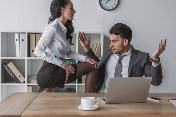 σέξι γραμματέας κάθεται στο γραφείο και δείχνει κάλτσα της κοντά σοκαρισμένος επιχειρηματίας - Φωτογραφία, εικόνα