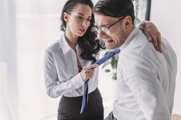 szexi titkárnő gazdaság nyakkendő és átöleli ijedt barátja, miközben elcsábítja őt az irodában - Fotó, kép