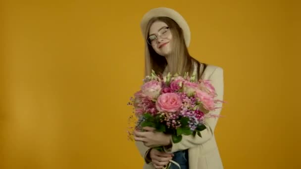 Stilvolle junge Frau in Brille, die mit einem Lächeln Blumen schnüffelt - Filmmaterial, Video