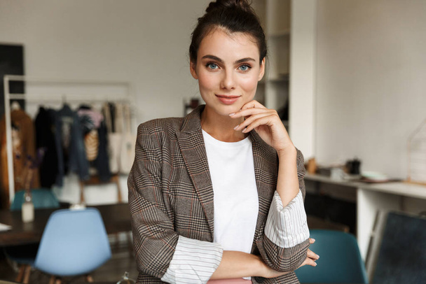 Atraktivní sebevědomá mladá žena návrhářka stojící v kanceláři, dívající se do kamery - Fotografie, Obrázek
