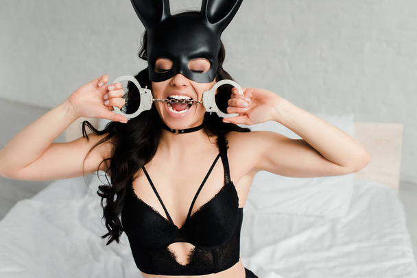 sexual female submissive in erotic rabbit mask biting handcuffs in bed - Фото, зображення
