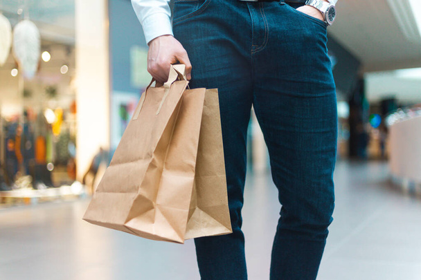 Großaufnahme eines jungen, stylischen Mannes, der in einem Einkaufszentrum mit umweltfreundlichen Einkaufstaschen in der Hand mit Waren und Kleidung spaziert. Verkauf, Discount, Konzept ausverkauft. Saisonausverkauf - Foto, Bild