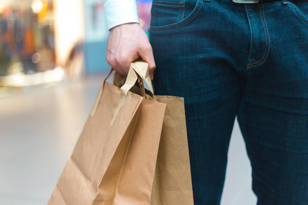 Detailní záběr mladého stylového muže kráčejícího v obchoďáku s ekologickými nákupními taškami v ruce se zbožím a oblečením. Prodej, sleva vyprodáno koncept. Sezónní vyprodání - Fotografie, Obrázek