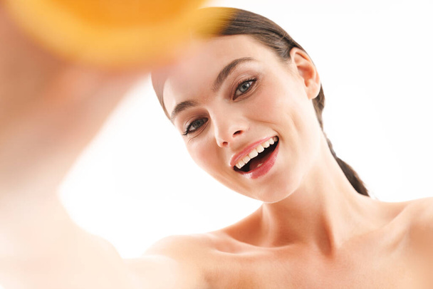 Beauty portret van een aantrekkelijke glimlachende jonge topless brunette vrouw geïsoleerd over witte achtergrond, tonen gesneden oranje - Foto, afbeelding