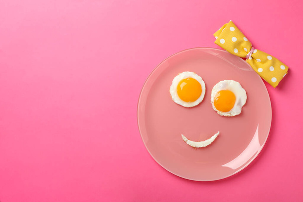 Glimlach gezicht gemaakt van plaat met gebakken eieren op roze achtergrond, bovenaanzicht - Foto, afbeelding