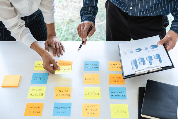 Two creative business people meeting and planning use post it notes sticky note on desk to share idea, Analysis data chart and graph with teamwork strategy brainstorming in office. - 写真・画像