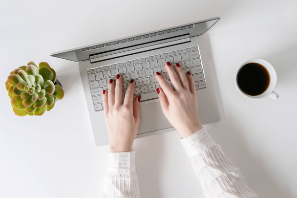 Woman freelancer working and typing on a  keyboard of laptop while sitting in an office at a table. Flat lay - Photo, Image