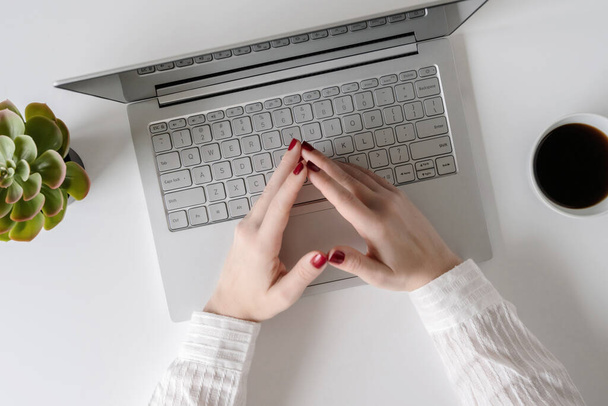 Nainen freelancer työskentelevät ja kirjoittaminen näppäimistö kannettavan tietokoneen istuessaan toimistossa pöydässä. Litteä
 - Valokuva, kuva