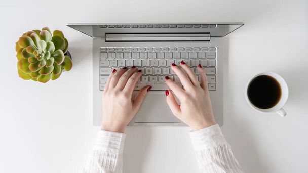 Woman freelancer working and typing on a  keyboard of laptop while sitting in an office at a table. Flat lay - Фото, зображення