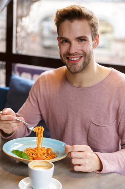 Smiling young man having lunch while sitting in the cafe indoors, eating pasta - 写真・画像