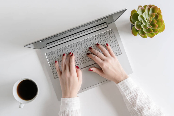 Woman freelancer working and typing on a  keyboard of laptop while sitting in an office at a table. Flat lay - 写真・画像
