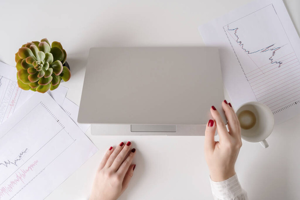 Kobieta freelancer wykończenie pracy i zamyka laptopa z pustym pić się filiżankę kawy i koniec dnia pracy. grafika i wykresy wydrukowane na papierze leżącym na stole. Układy płaskie - Zdjęcie, obraz