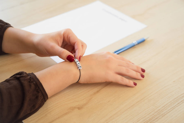 Student girl hand with bracelet and love word. Empty examination paper sheet on the table. First love during university exam. Concept - Foto, imagen