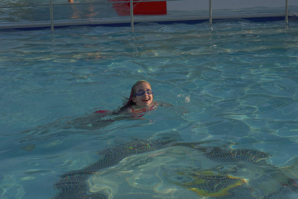 Schattig meisje met bril in het zwembad. Meisje zwemt in het zwembad met een bril. Zomer, zwembad, ontspanning, waterpark, ontspanningsruimte. De baby zwemt. Hallo zomer. Hoera, feestdagen. gezondheid - Foto, afbeelding