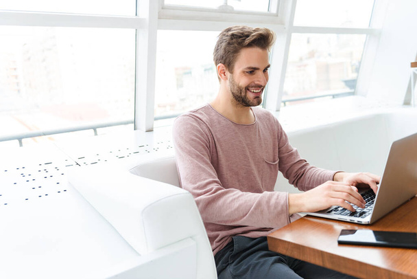 Зображення молодого бородатого чоловіка, який працює на ноутбуці, сидячи в кафе в приміщенні
 - Фото, зображення