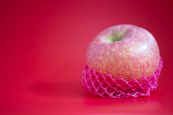 Fresco di mela avvolto con rete di frutta in schiuma su sfondo rosso
. - Foto, immagini