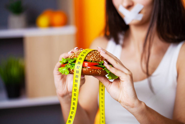 The concept of diet woman with sealed mouth keeps greasy burger - Foto, Bild