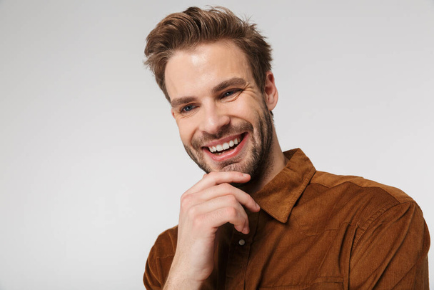 Portrait of cheerful young man wearing brown shirt posing at camera and smiling isolated over white background - Valokuva, kuva