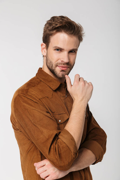 Portrait of unshaven young man wearing brown shirt posing and looking at camera isolated over white background - Foto, imagen