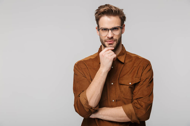 Portrait of unshaven young man wearing eyeglasses posing and looking at camera isolated over white background - Foto, Imagem