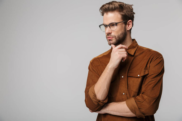 Portrait of unshaven young man wearing eyeglasses posing at camera and looking aside isolated over white background - Foto, Imagem