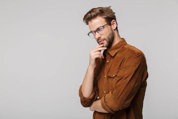 Portrait of unshaven young man wearing eyeglasses posing and looking at camera isolated over white background - Foto, immagini