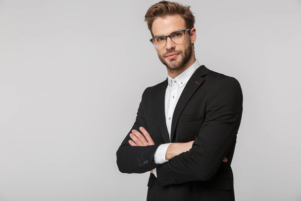 Portrait of handsome young businessman in eyeglasses posing and looking at camera isolated over white background - Foto, Imagen