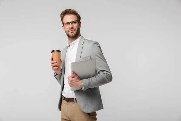 Portrait of serious handsome man in eyeglasses posing with laptop and paper cup isolated over white background - Valokuva, kuva