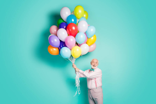 Portrait of positive cheerful old man hold many helium balloons fly air sky enjoy festive occasion wear pink trousers isolated over teal color background - Φωτογραφία, εικόνα