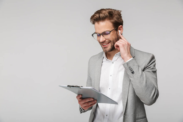 Portrait of happy handsome man in eyeglasses using earphones and holding clipboard isolated over white background - Φωτογραφία, εικόνα