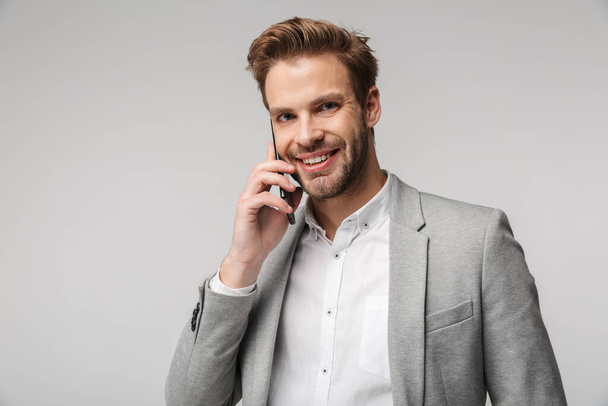 Portrait of happy handsome man in jacket talking on cellphone and smiling isolated over white background - Photo, Image