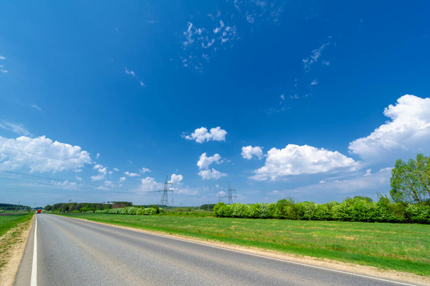 jarní fotografie pořízena širokoúhlou čočkou, místní dálnice, jasně zelené stromy, mraky na modré obloze - Fotografie, Obrázek